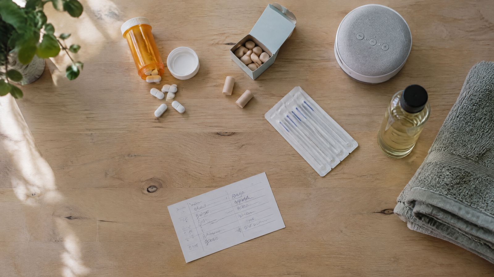Pills, earplugs, a white-noise speaker, acupuncture needles and massage oil on a table